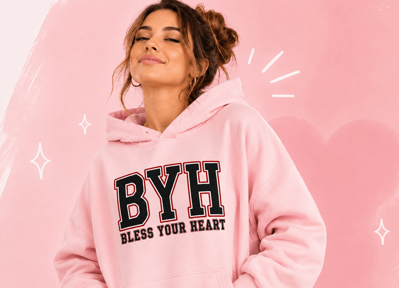 Woman wearing a pink “BYH Bless Your Heart” hoodie against a pink graphic background.